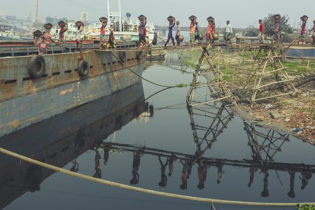 Workers transporting baskets of coal on the top of their heads along planks of wood Coal workers in Dhaka, Bangladesh transporting baskets of coal across the bridge.
