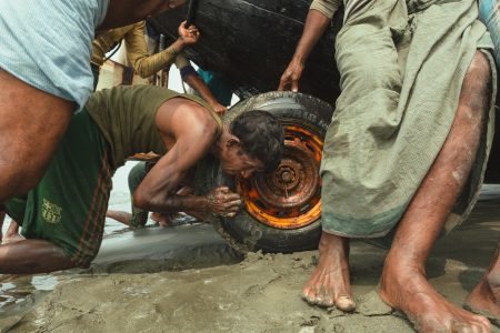 Fishers working together to lift a wooden boat out of a sandpit Forcing a bogged boat out of the wet sand and Bay of Bengal, Cox’s Bazar Bangladesh