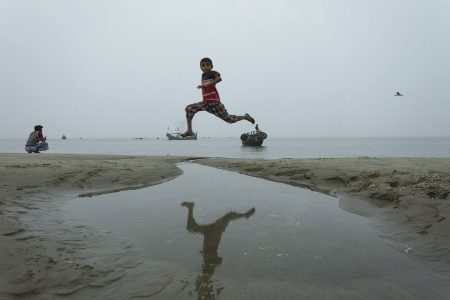 A jumping boy jumps across a puddle of water on the Bay of Bengal A child leaping over puddles in the sand at Bay of Bengal, Cox’s Bazar Bangladesh