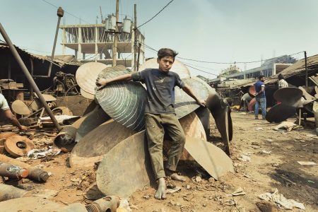 A young worker takes a minor rest leaning against spare parts for repairing the ships. Boy resting against spare parts at Dhaka, Bangladesh Shipyard.