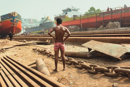 A young and fit worker watches as a new ship arrives at the Shipyard for repairs via the tracks. Viewing arrival of new repair project at Dhaka, Bangladesh Shipyard.