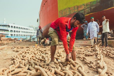 With other workers exploring solutions, this man strains to move huge metal anchor chains. With other workers exploring solutions, this man strains to move huge metal anchor chains. Worker struggling to move chains at Dhaka, Bangladesh Shipyard.