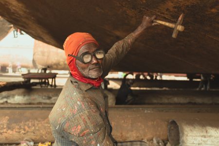 Between 12 to 16 hours a day, his hammer among a thousand banging incessantly against massive ship bodies to remove rust. Protective eye and headwear for some metal work activities at Dhaka, Bangladesh Shipyard.