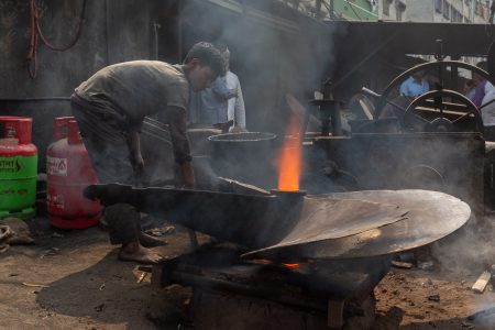 The danger and heat of this environment highlight the urgent risks faced by child labourers in Bangladesh’s industrial zones. A barefoot young boy works in the hazardous conditions of a shipyard in Dhaka, Bangladesh. Surrounded by smoke and intense heat, he leans over a large metal structure as flames rise from molten material. His worn-out clothing and focused expression highlight the dangers and harsh realities of child labour in heavy industry. In the background, towering machinery and gas cylinders add to the scene's intensity, emphasizing the risks these children face daily.